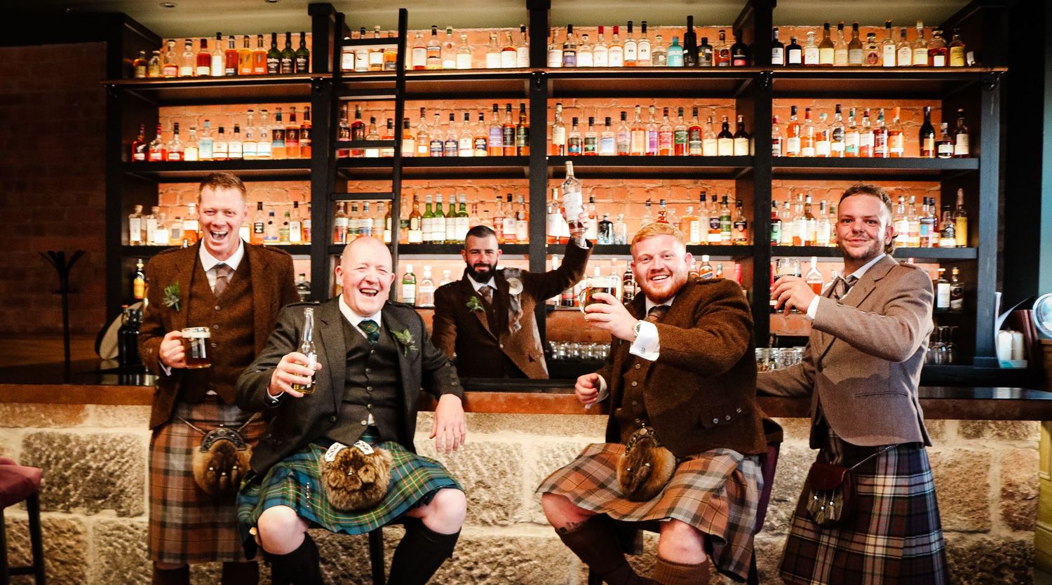 Bar patrons and staff gather at a dimly lit wooden bar counter for drinks and conversation at a cozy pub.