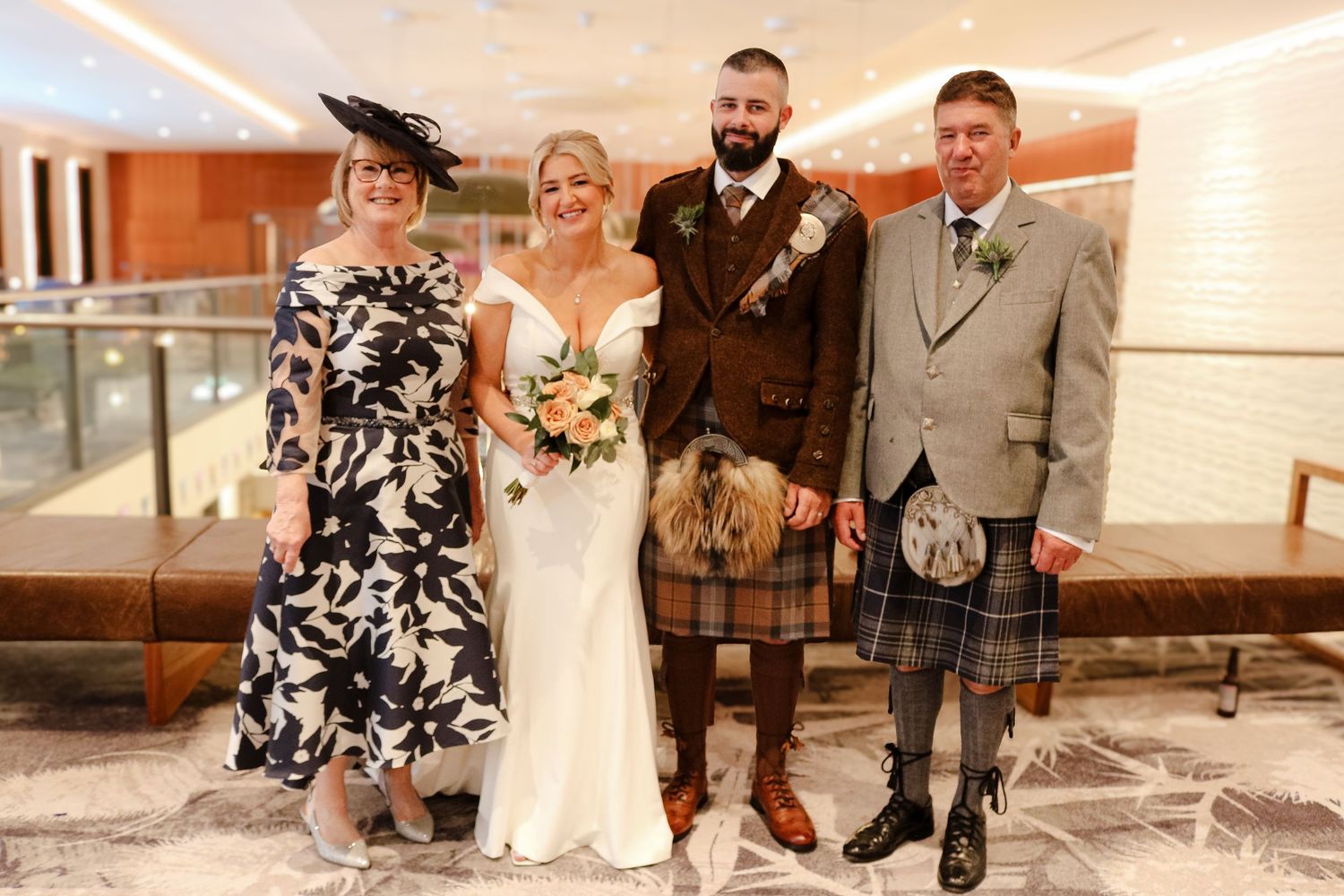 Formal wedding party in traditional Scottish attire including kilts poses together in an indoor venue.