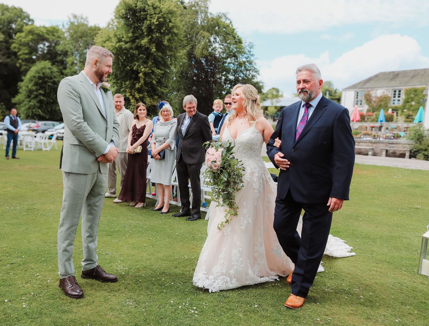 Outdoor wedding ceremony on a bright sunny day with guests gathered on a green lawn.