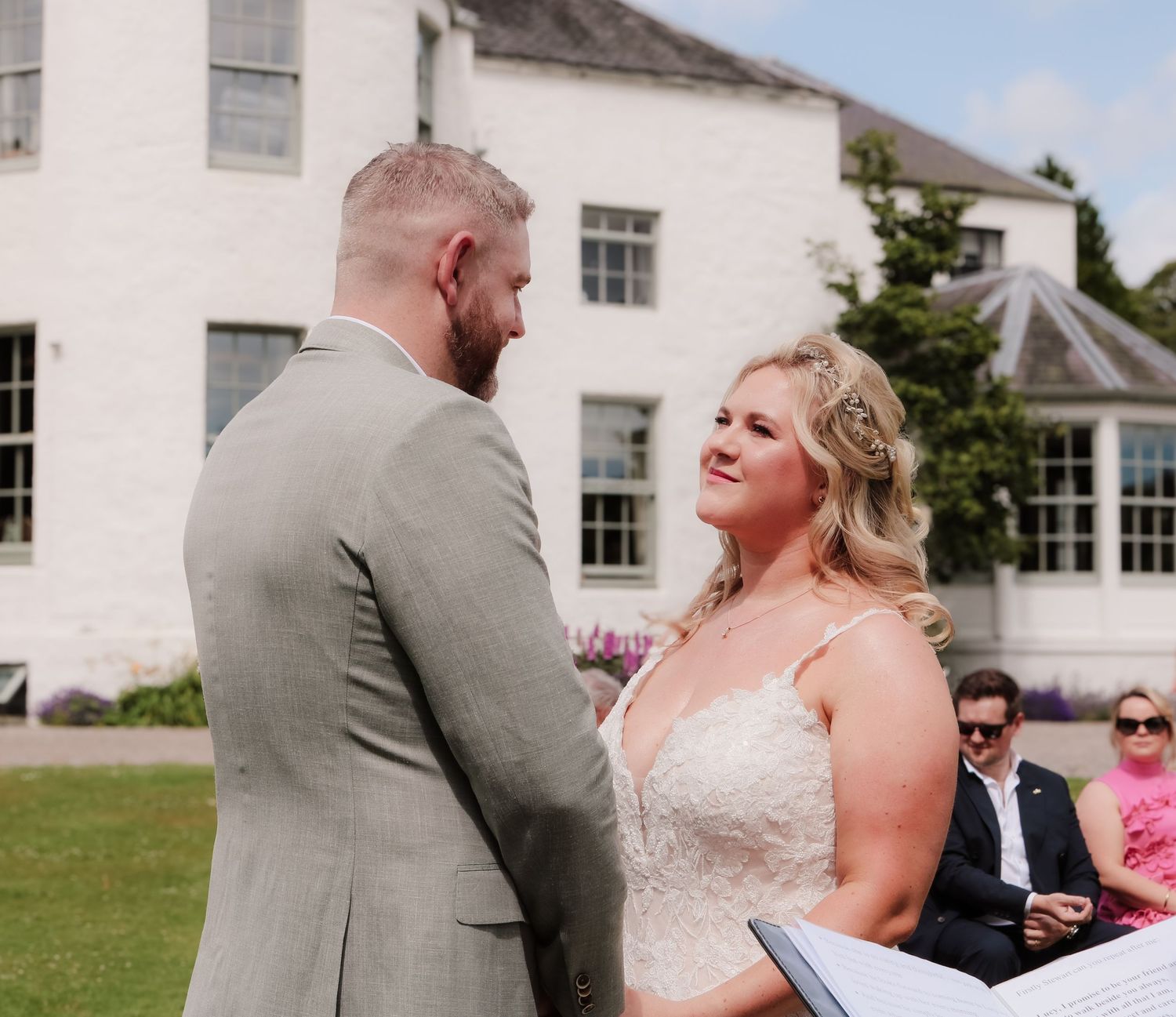 A bride and groom share a moment during their outdoor wedding ceremony in front of a white historic building.
