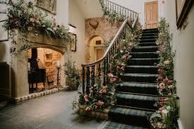 A grand stone staircase decorated with floral arrangements and holiday greenery leads up from an elegant entryway with lit sconces.