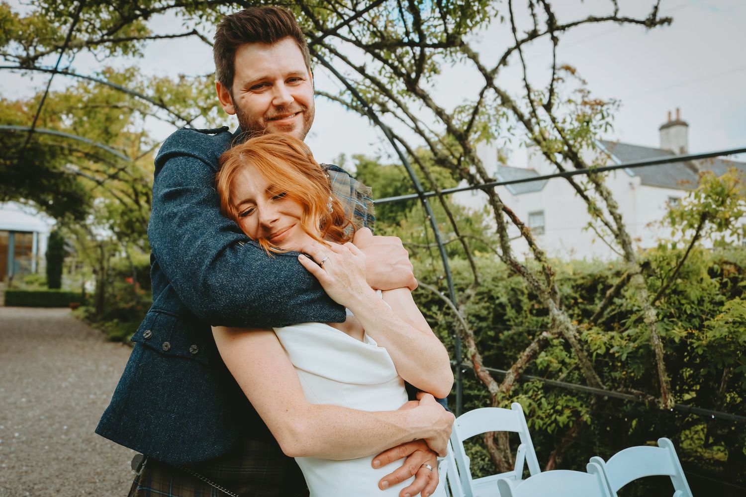 A romantic couple shares an intimate embrace in front of blooming trees and church during an outdoor wedding celebration.