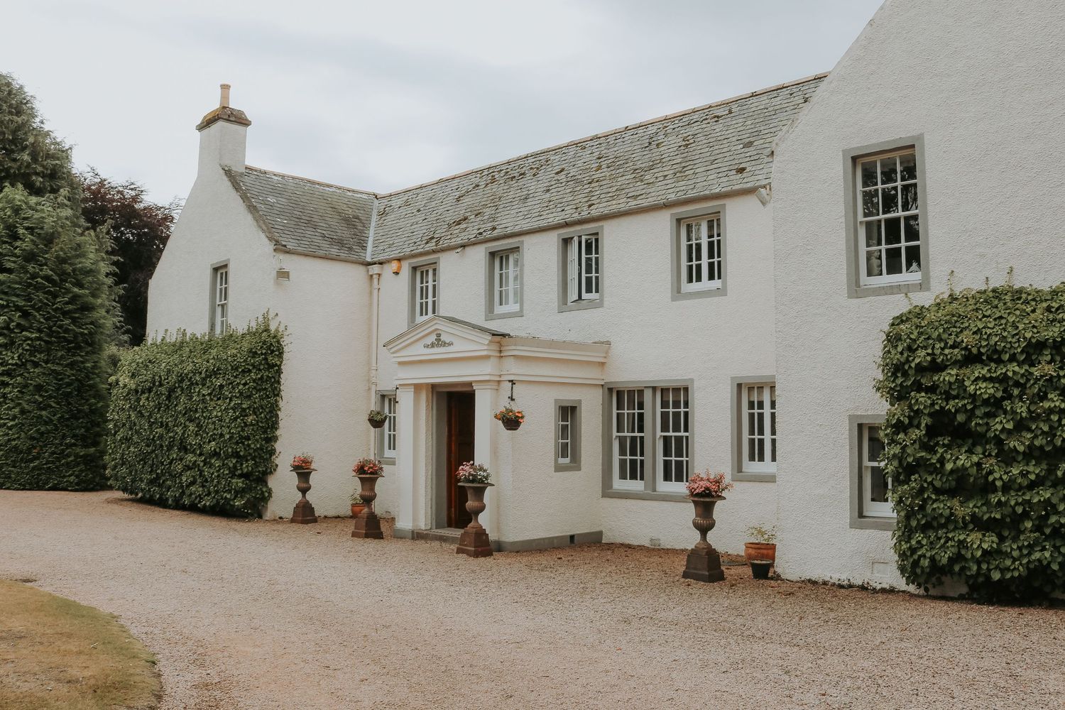 White country house with multiple windows and symmetrical design features climbing vines and potted plants at entrance.