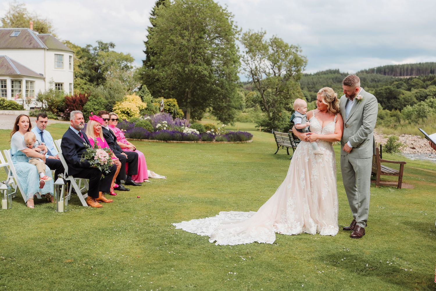 Wedding party poses on a scenic grassy hillside during an outdoor summer celebration.