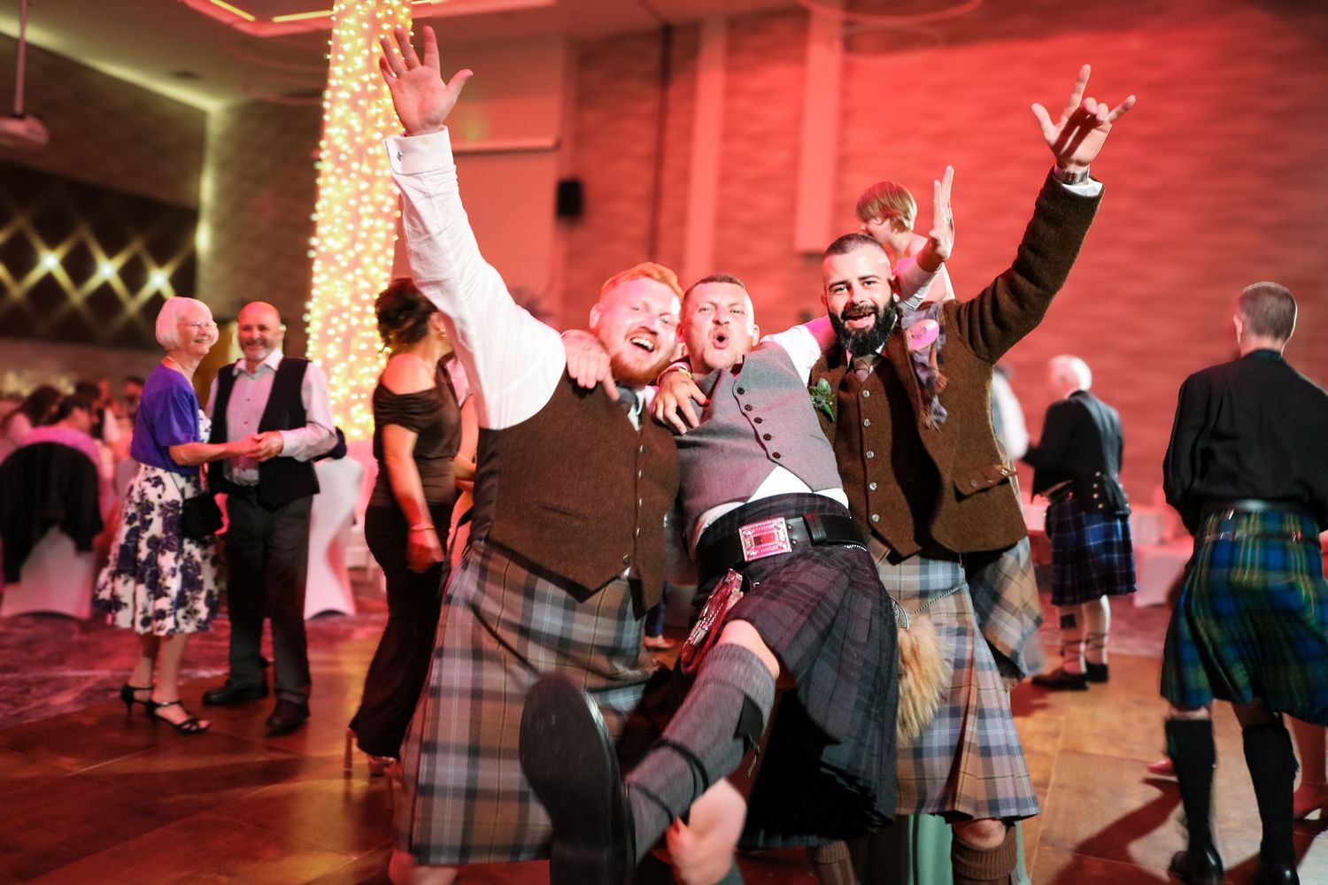 Couples dancing together at an evening event with red ambient lighting and festive decorations.