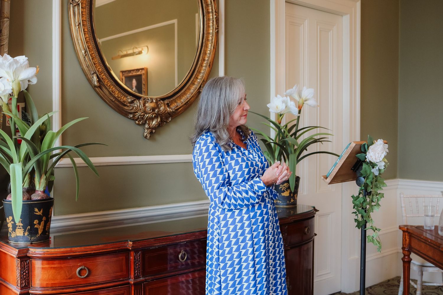 About to put lovely white lilies on display in corner cabinet, with ornate gold mirror on wall.