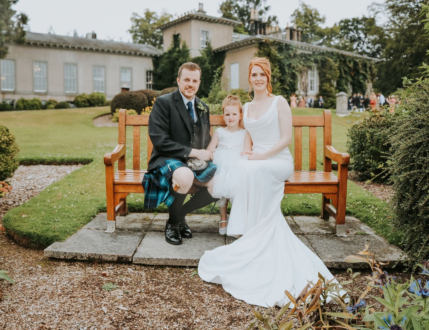 A couple sitting together on a wooden outdoor bench in front of a garden setting.