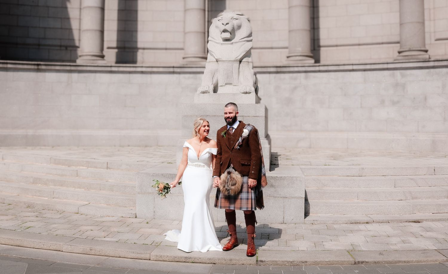 A bride and groom stand together on stone steps outside an ornate building.