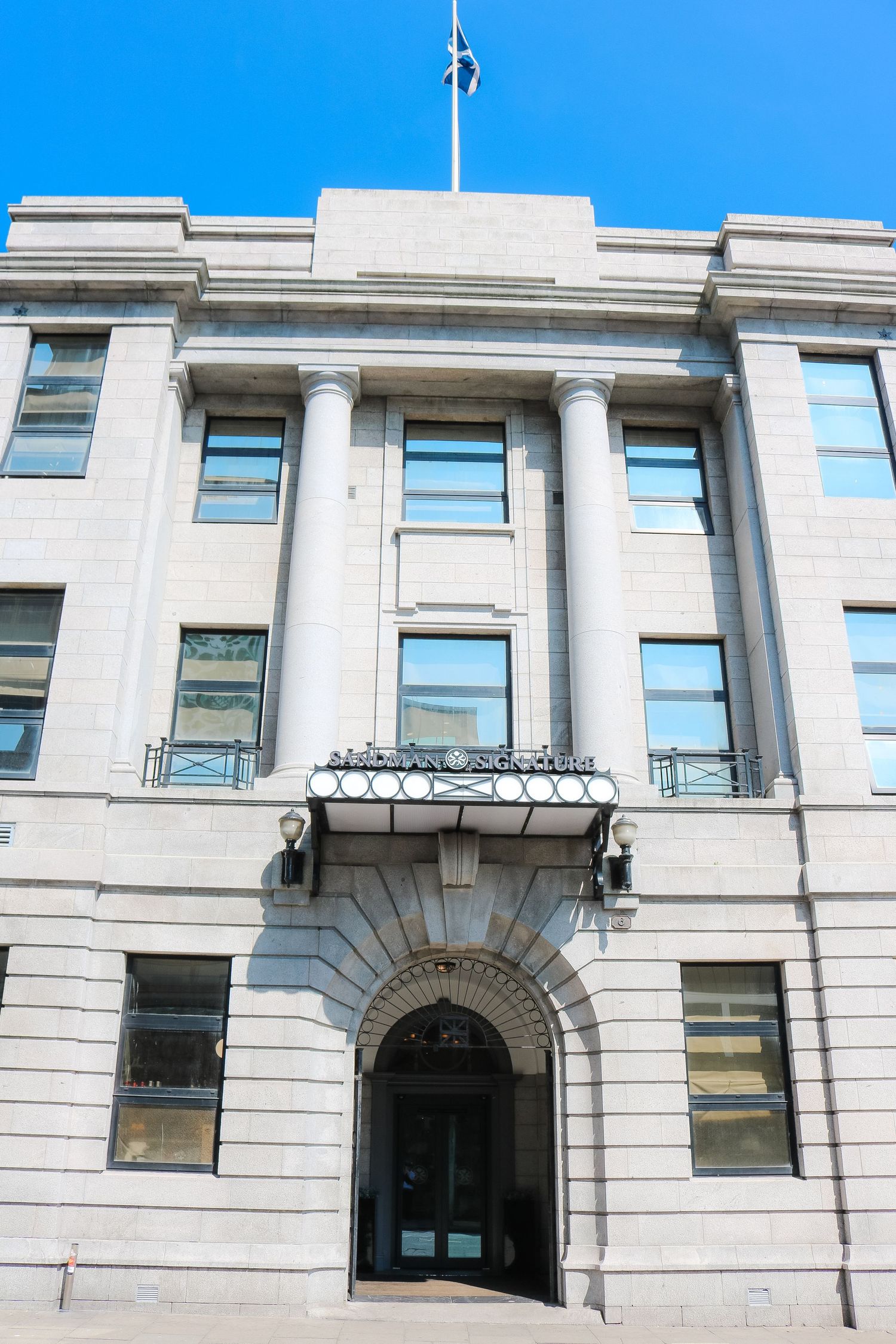 Neoclassical white stone building facade with arched entrances and windows along a continuous exterior wall.