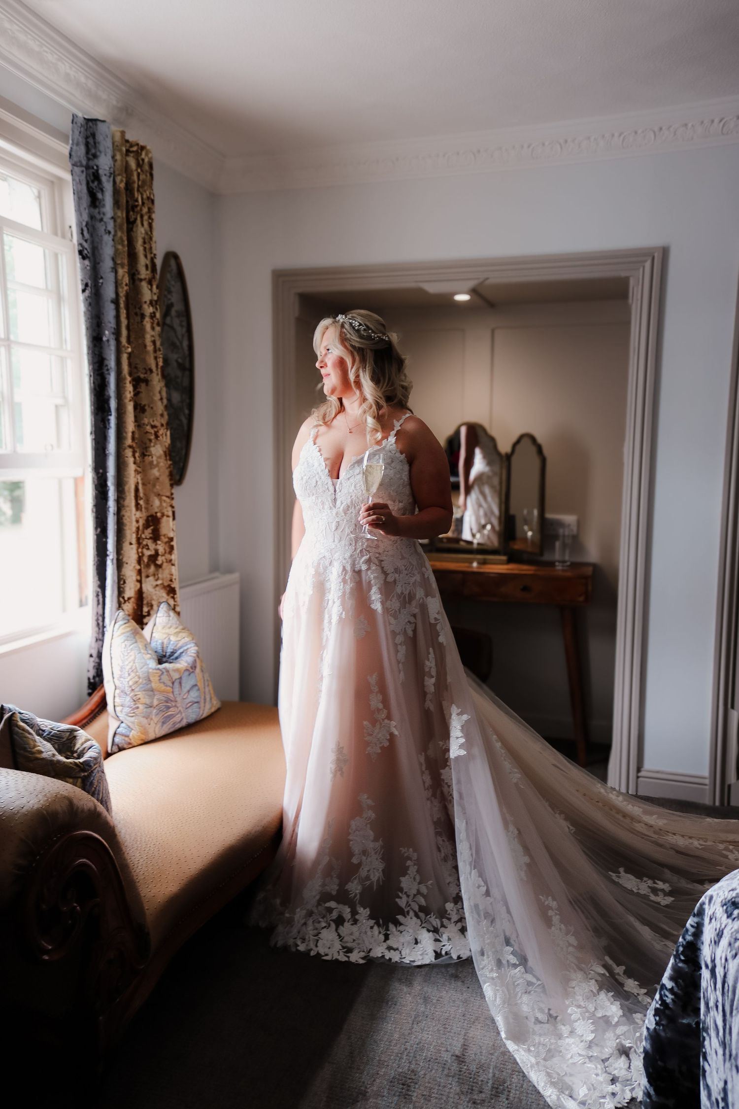 Sunlit bridal suite room showing a flowing lace wedding dress and delicate veil in elegant indoor setting.