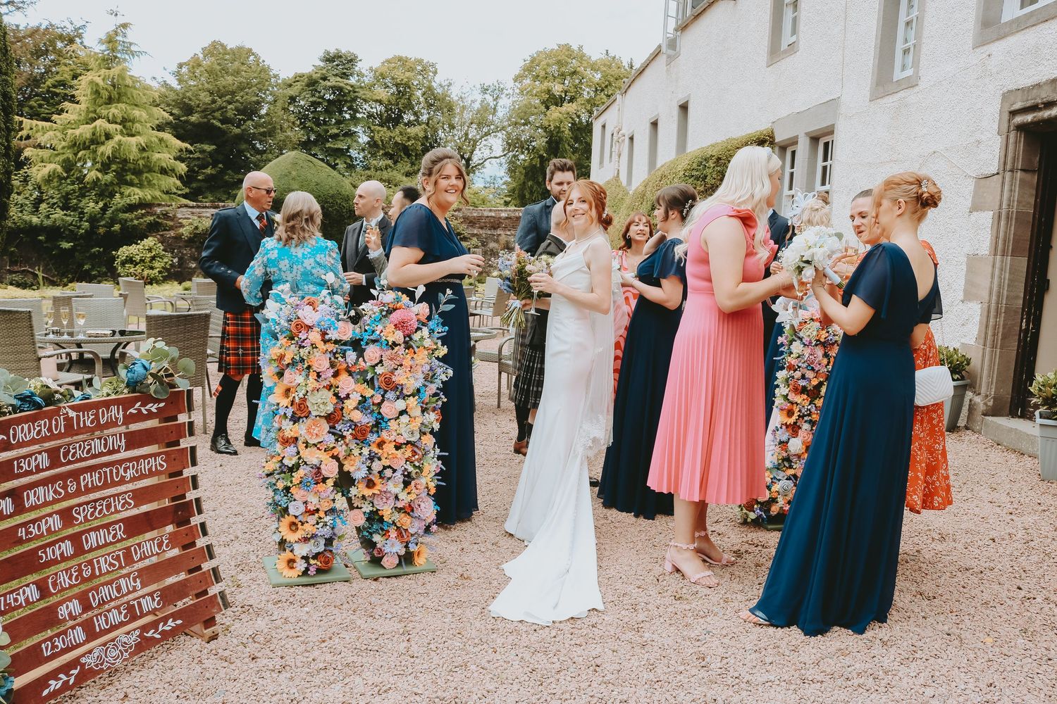 Wedding party in formal attire gathered outside historic brick building during outdoor celebration ceremony.