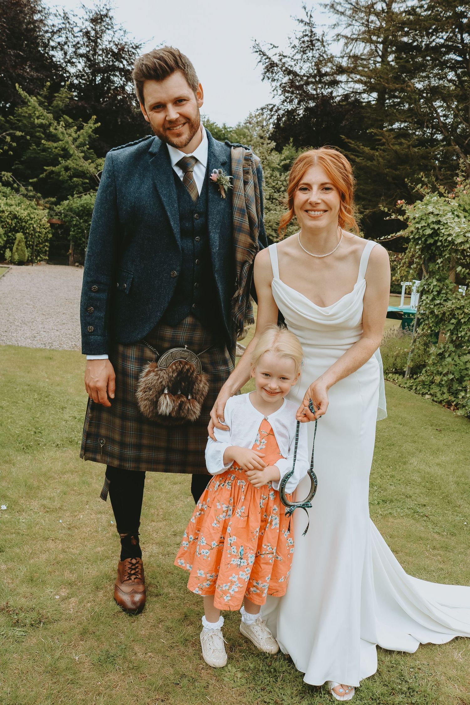 A heartwarming outdoor wedding scene captures smiles and laughter as a small child in an orange dress joins the celebration.