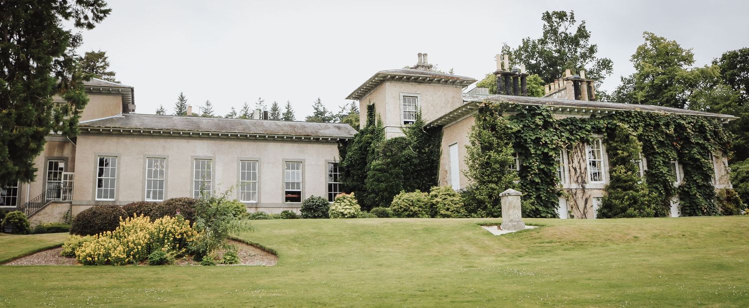 Elegant historic manor house with ivy-covered walls and manicured lawn in countryside setting.