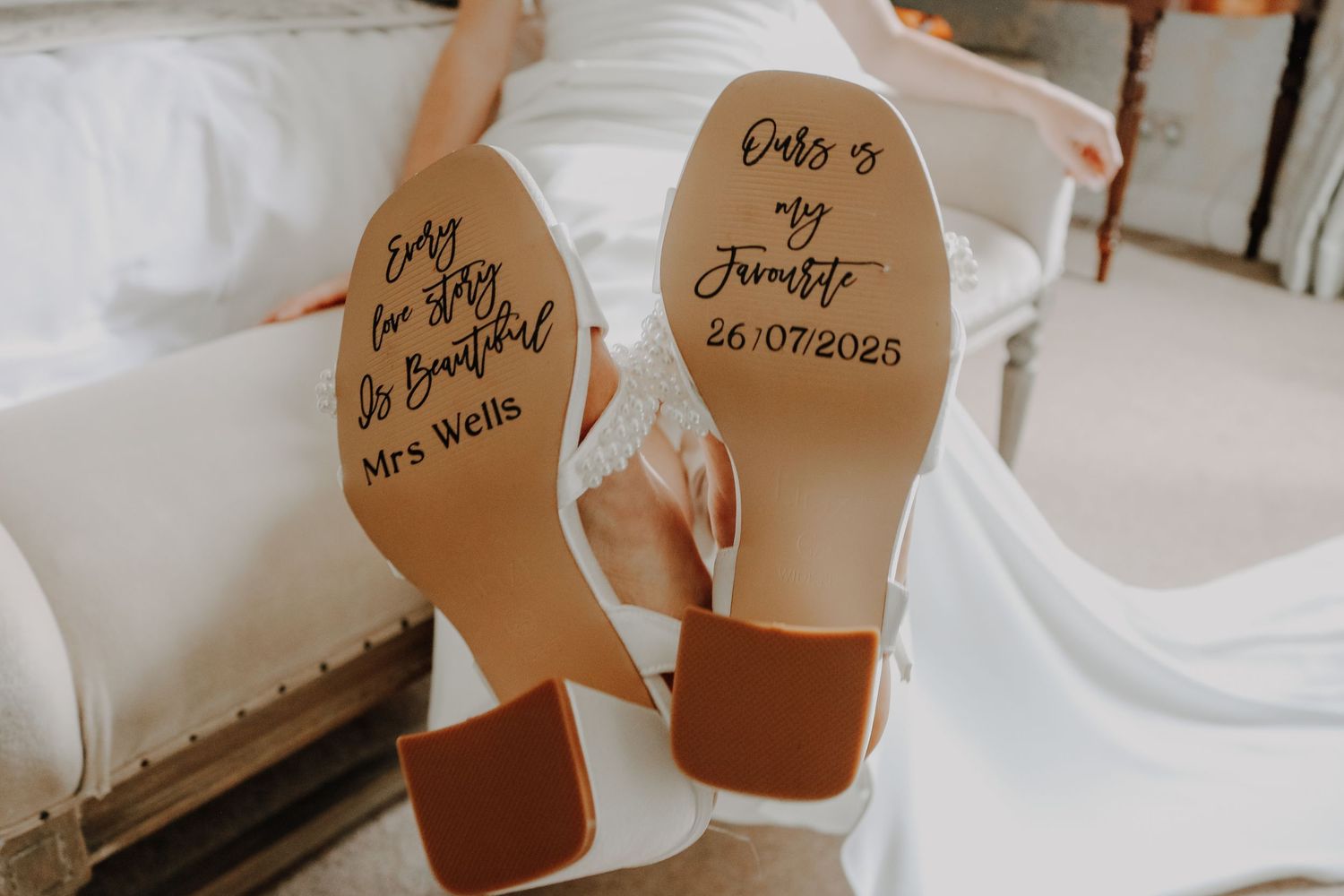 Wedding shoes with handwritten message inscribed on the soles laid on white fabric.
