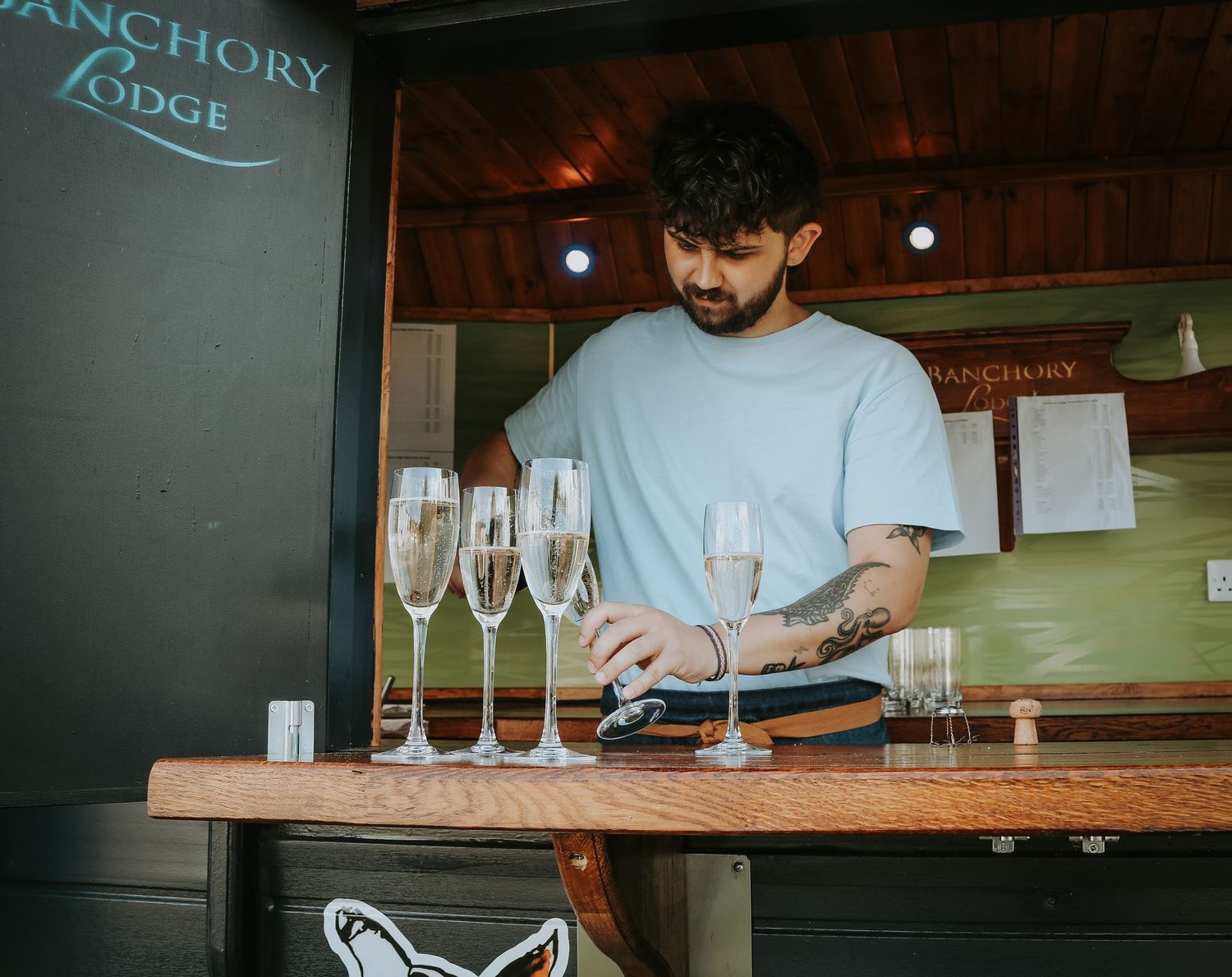 Bartender carefully pours drinks at a rustic wooden bar with glasses lined up for service.