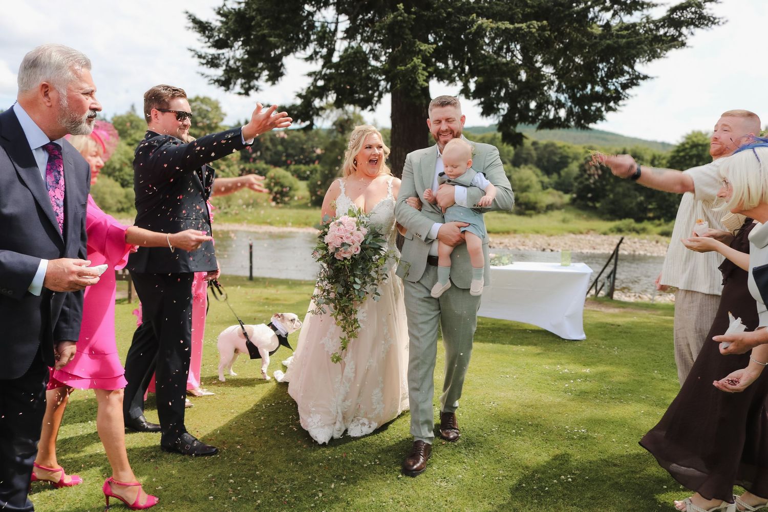 Wedding guests showering the happy couple with confetti on a lush lawn overlooking a scenic coastal view.