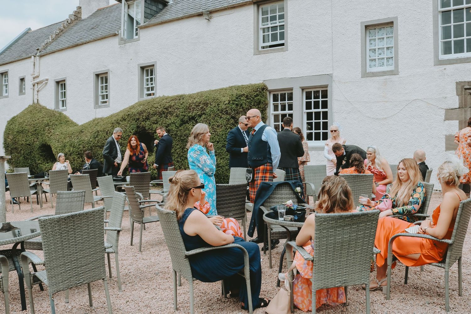 A series of wedding reception photos showing guests sitting and mingling at an outdoor venue with white stone buildings.