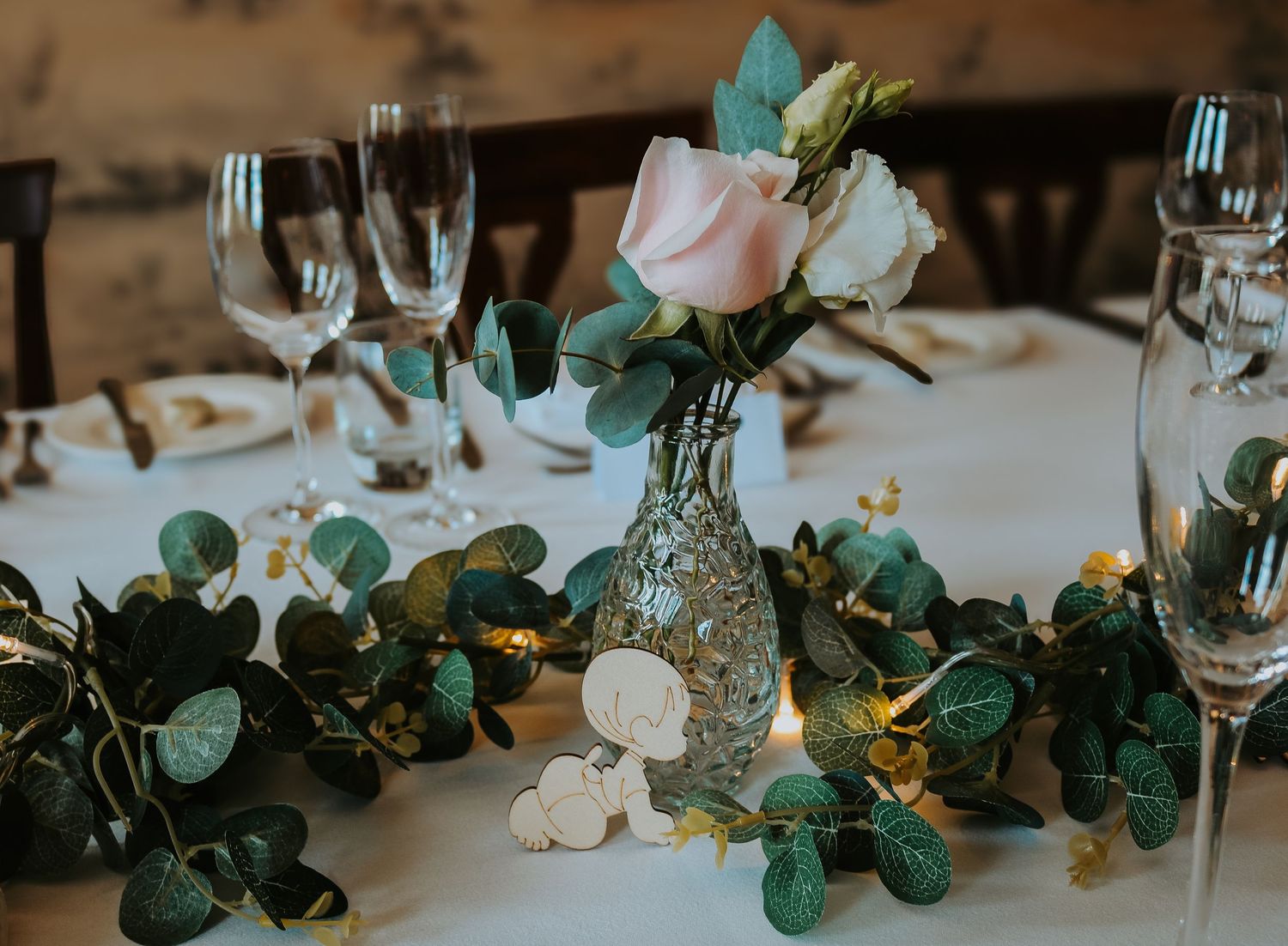 Wedding reception table decor features elegant eucalyptus garland with twinkle lights and place settings.