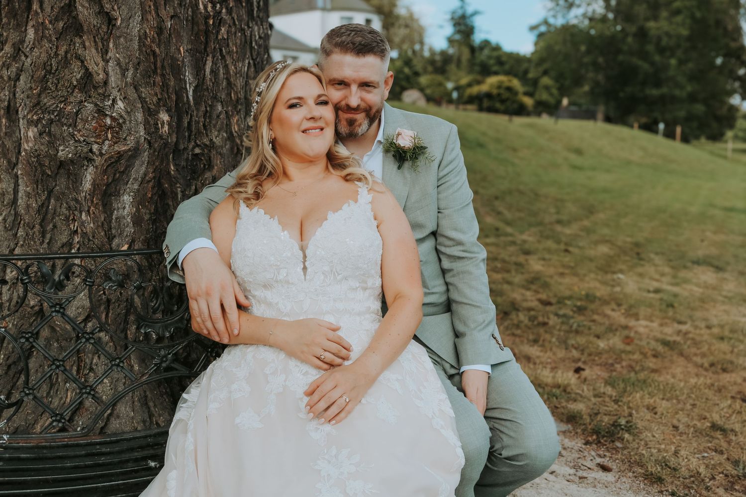A newlywed couple share an intimate moment together while sitting against a large tree trunk outdoors.