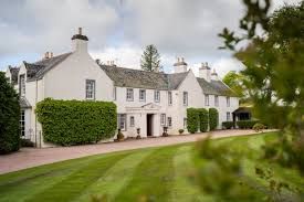 Traditional white harled Scottish country house with manicured lawn and neat hedgerows on curved driveway.