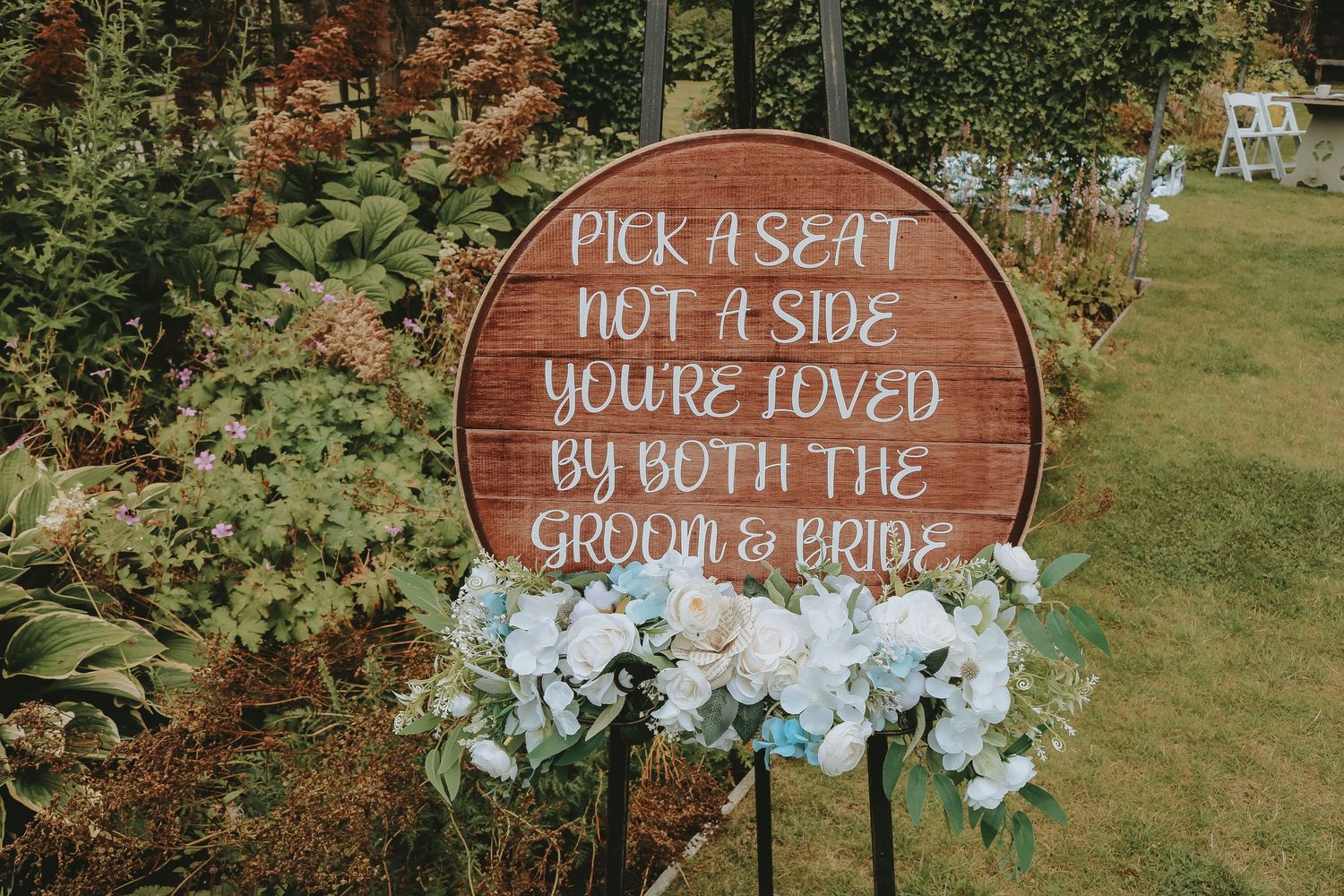 Wooden wedding signs with white floral decor display loving messages against a natural outdoor background.