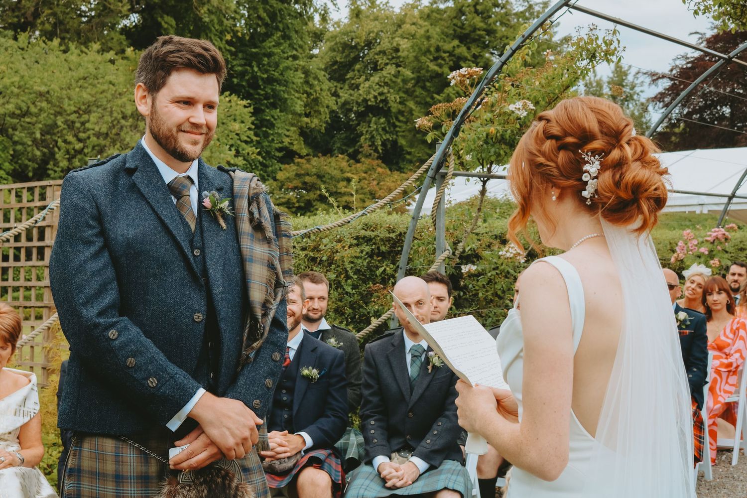 Scottish wedding ceremony takes place outdoors with the groom wearing traditional kilt attire.