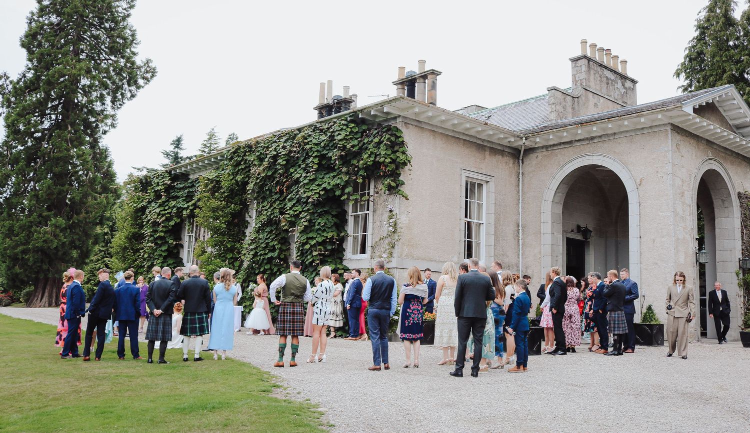 A panoramic sequence shows guests gathering outside an elegant stone mansion during an outdoor event or celebration.