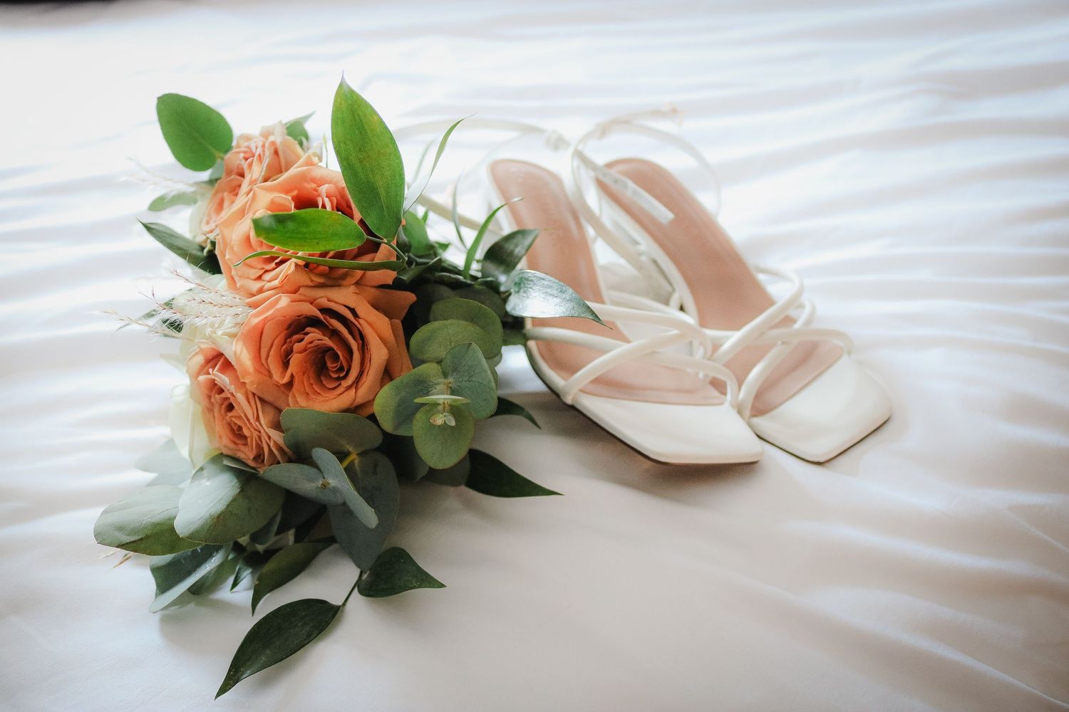 White ballet shoes and a peach-colored rose displayed on crisp white bedding.