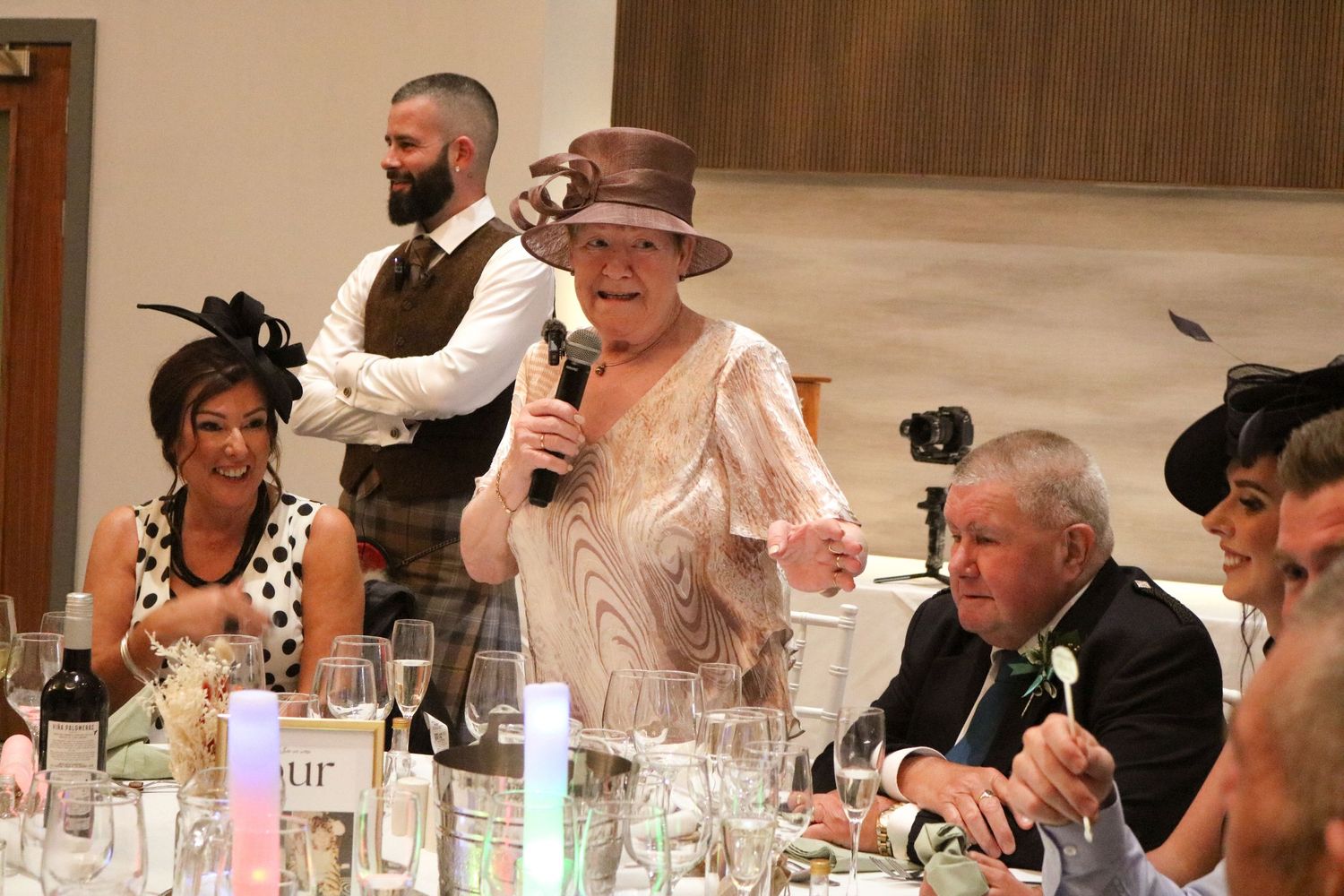 People gathered at a banquet table for a formal dinner event with guests in formal attire speaking into a microphone.
