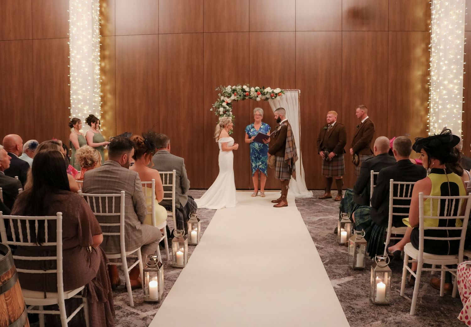 Wedding ceremony in an elegant ballroom with wooden panels and white chiavari chairs lining the aisle.