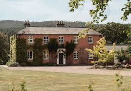 Large red brick Georgian manor house with symmetrical windows and a manicured lawn in the countryside.