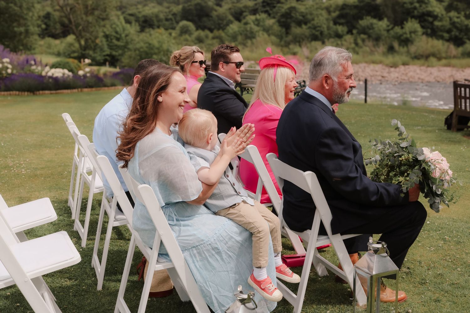 Wedding guests seated in white folding chairs on a grassy lawn during an outdoor ceremony.