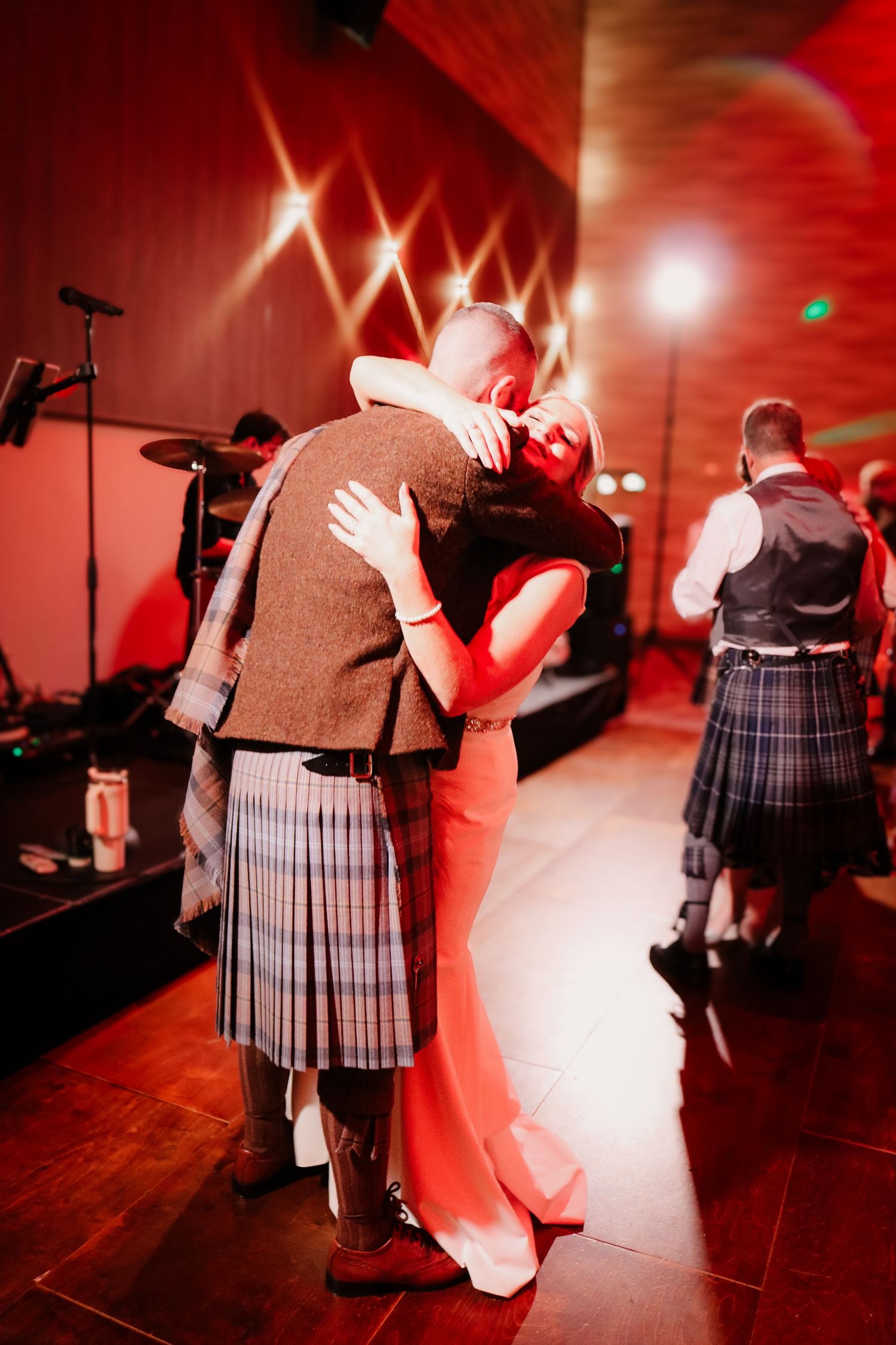 Dancers perform a traditional Scottish wedding dance in a ballroom bathed in dramatic red lighting and atmospheric fog.
