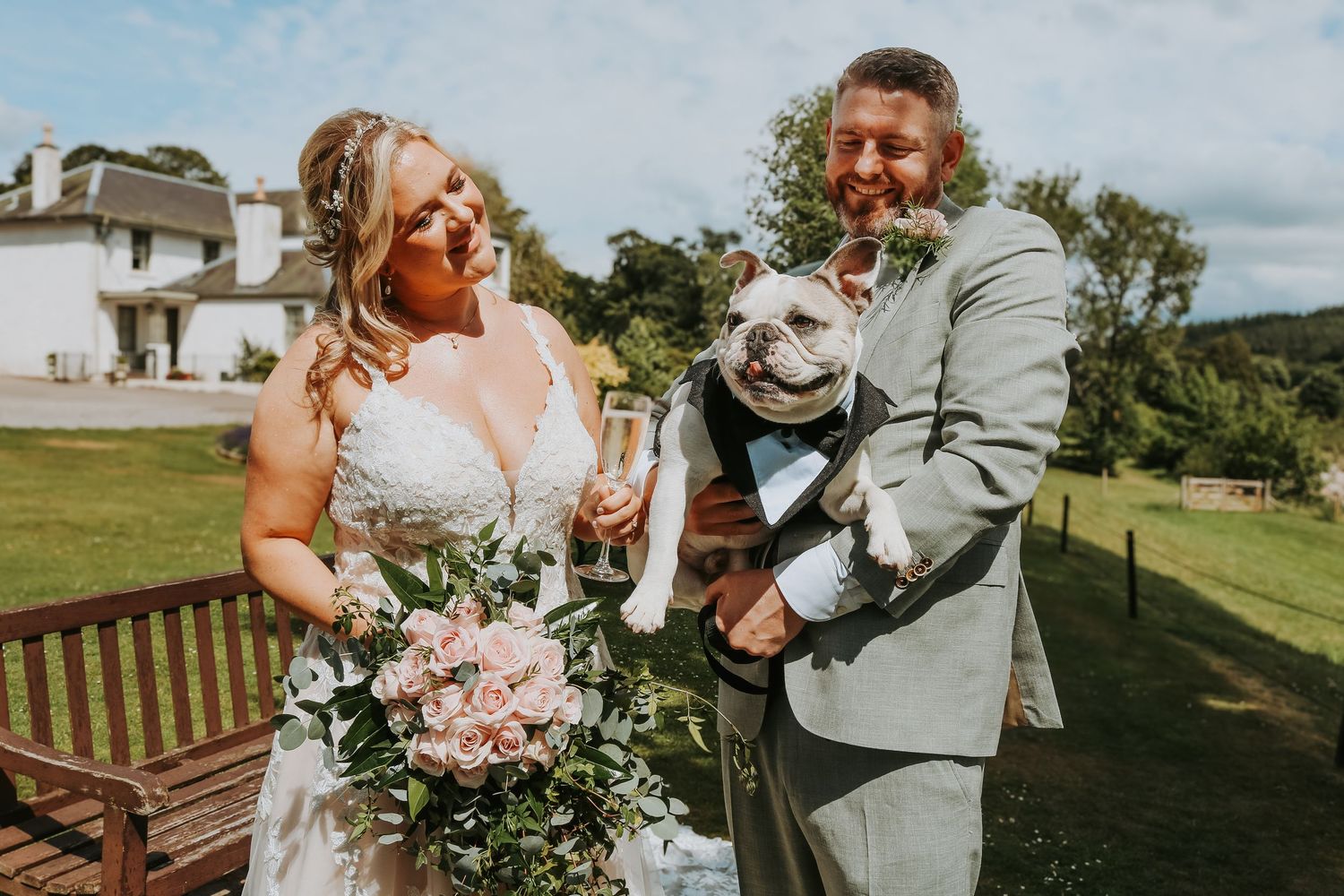 Outdoor wedding party poses with bouquets on a sunny day against green rolling hills.