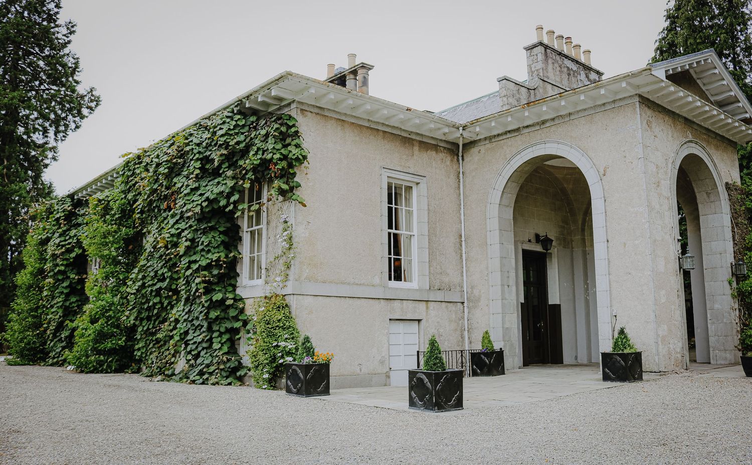 Historic white stone mansion exterior features elegant arched doorways and columns along a curved colonnade walkway.