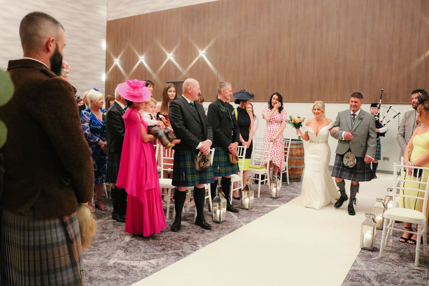 Wedding guests seated in rows at an indoor ceremony venue wave their arms in celebration during a special moment.
