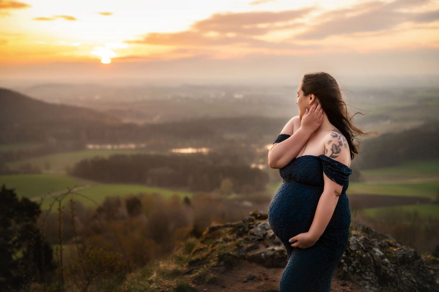 A silhouette in a flowing dress stands on a hilltop overlooking a misty valley at sunset.