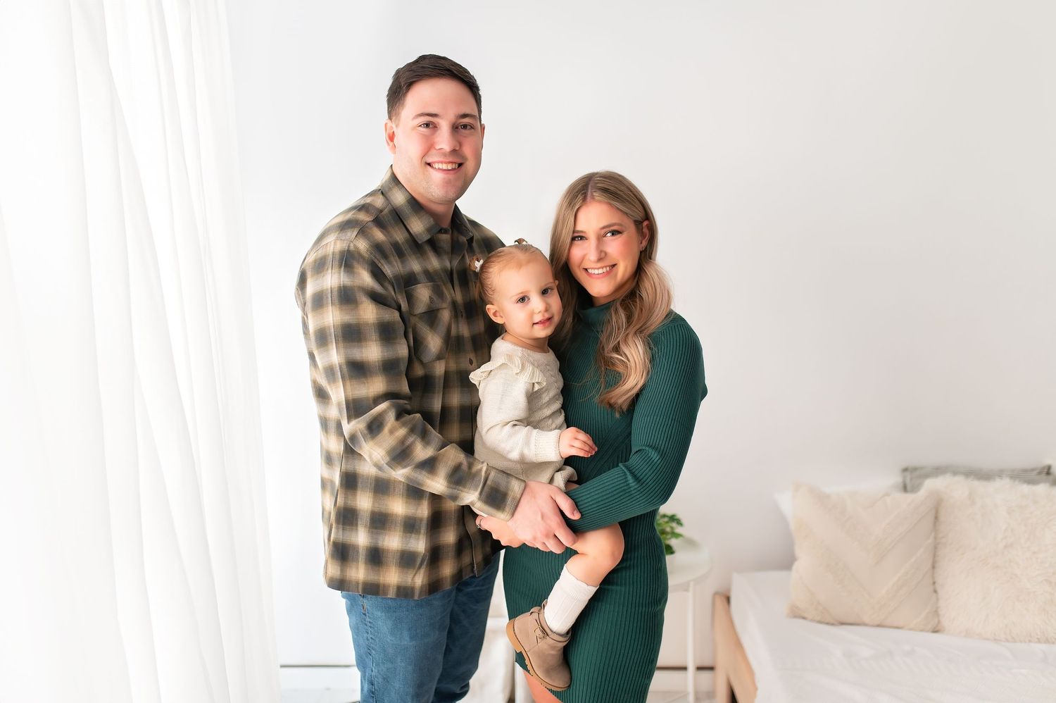 Family posing together in casual attire against neutral home backdrop.