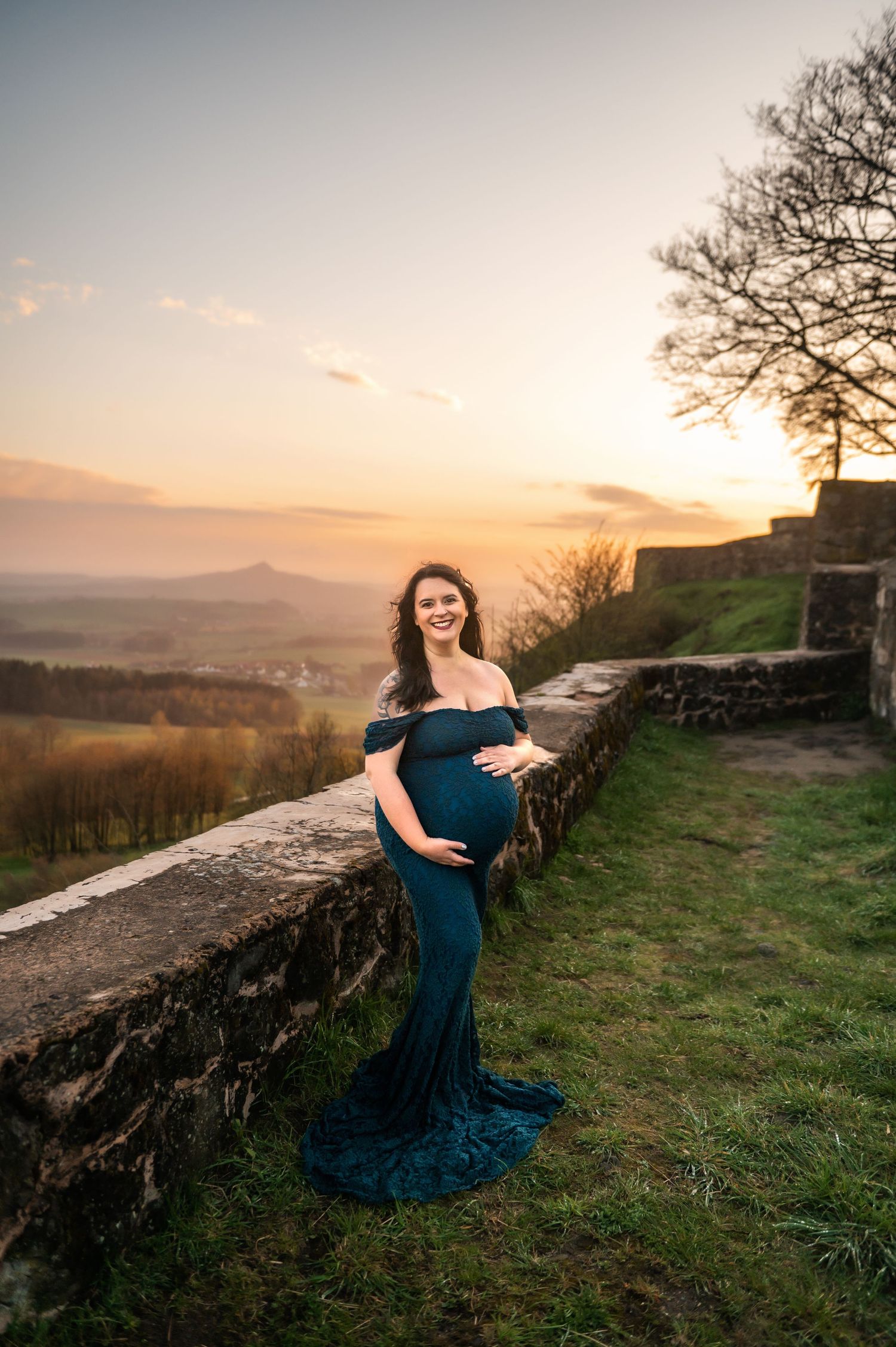 Maternity session at sunset featuring woman in blue dress against mountain backdrop.