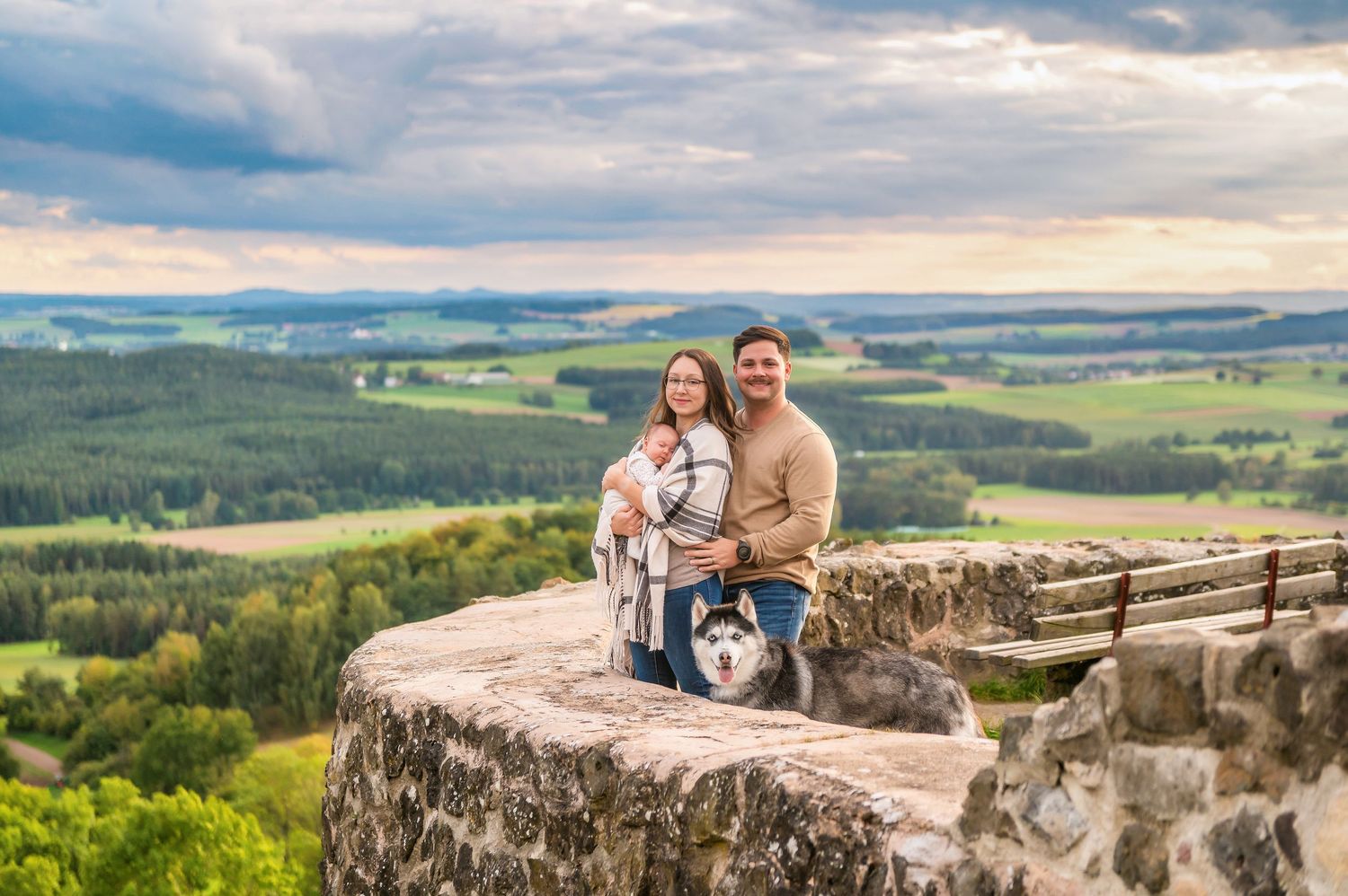 A group poses with their dog on a scenic mountain overlook during golden hour.