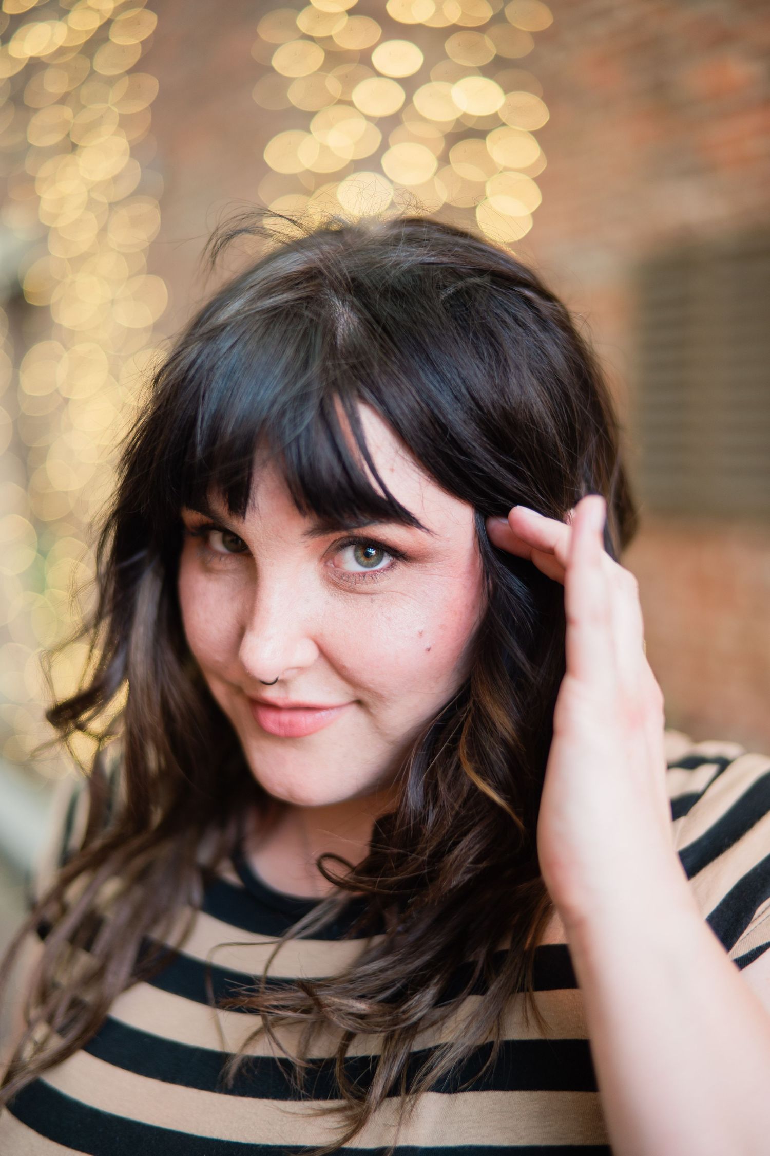 Portrait with dark wavy hair and striped shirt against blurred bokeh lights in background.