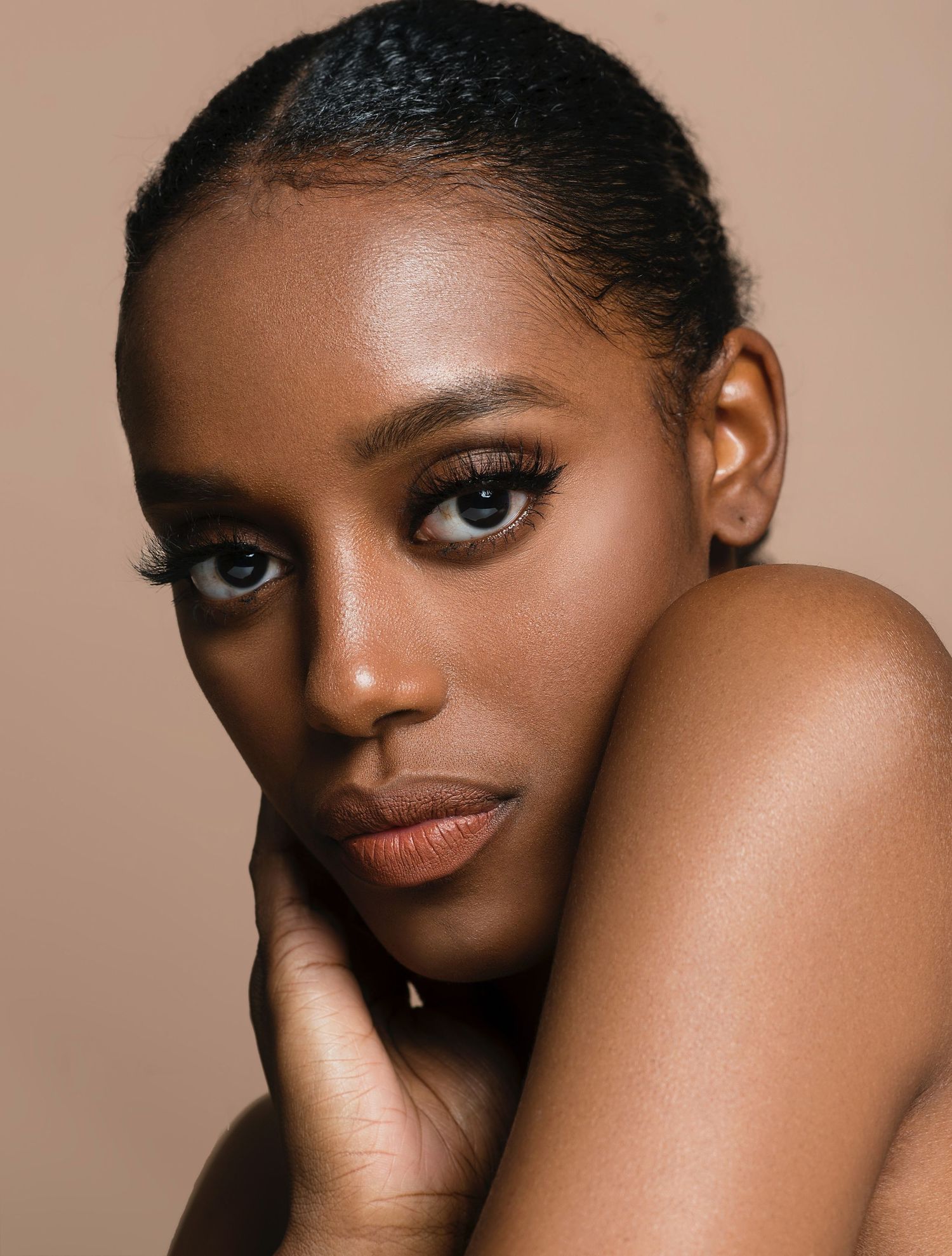 Beautiful close-up beauty portrait with glowing skin and natural makeup against a neutral beige background.