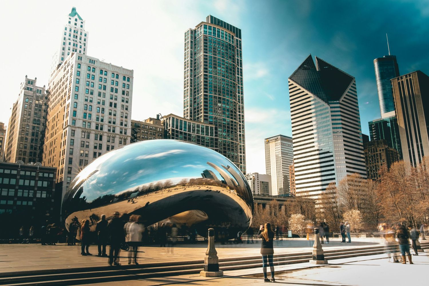 Urban panorama of Chicago skyline and Cloud Gate sculpture reflecting modern buildings and blue sky in Millennium Park.