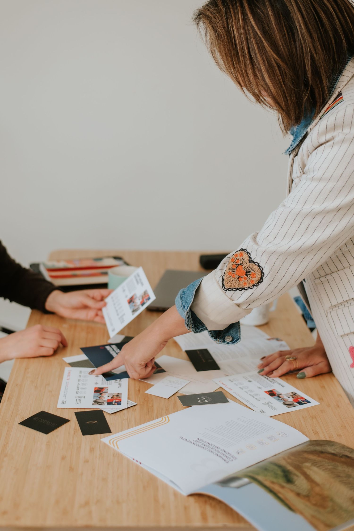 People working together at wooden table with papers and photographs spread out during collaborative meeting session.
