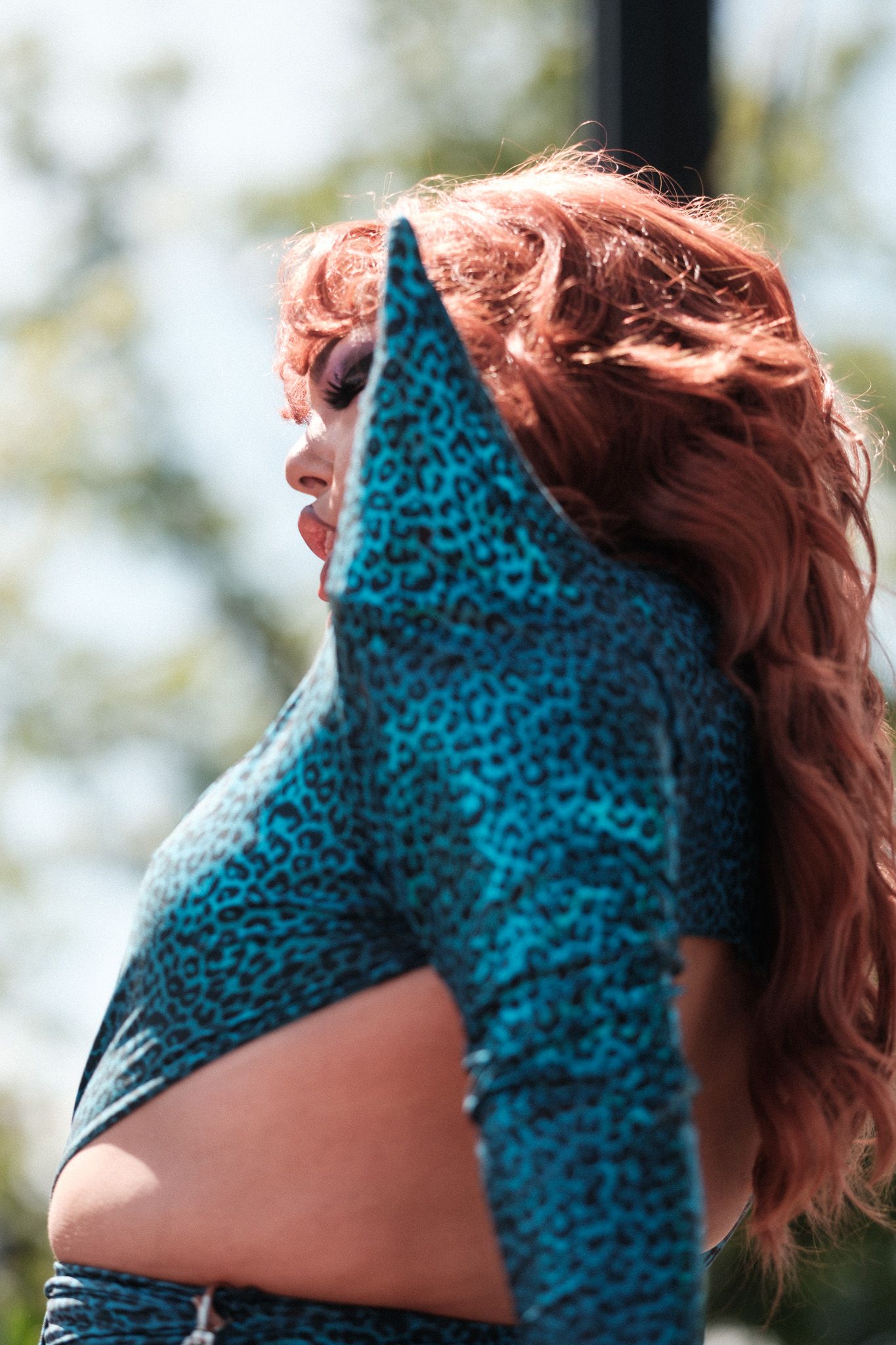 A person with red hair wearing a turquoise and black patterned top stretches in an outdoor setting.