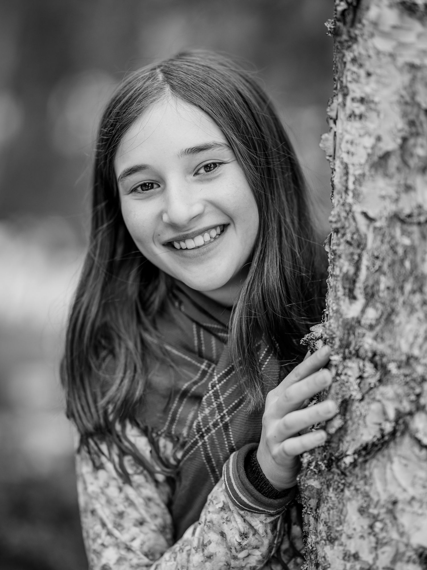 Black and white portrait next to a birch tree trunk with a natural, joyful expression.