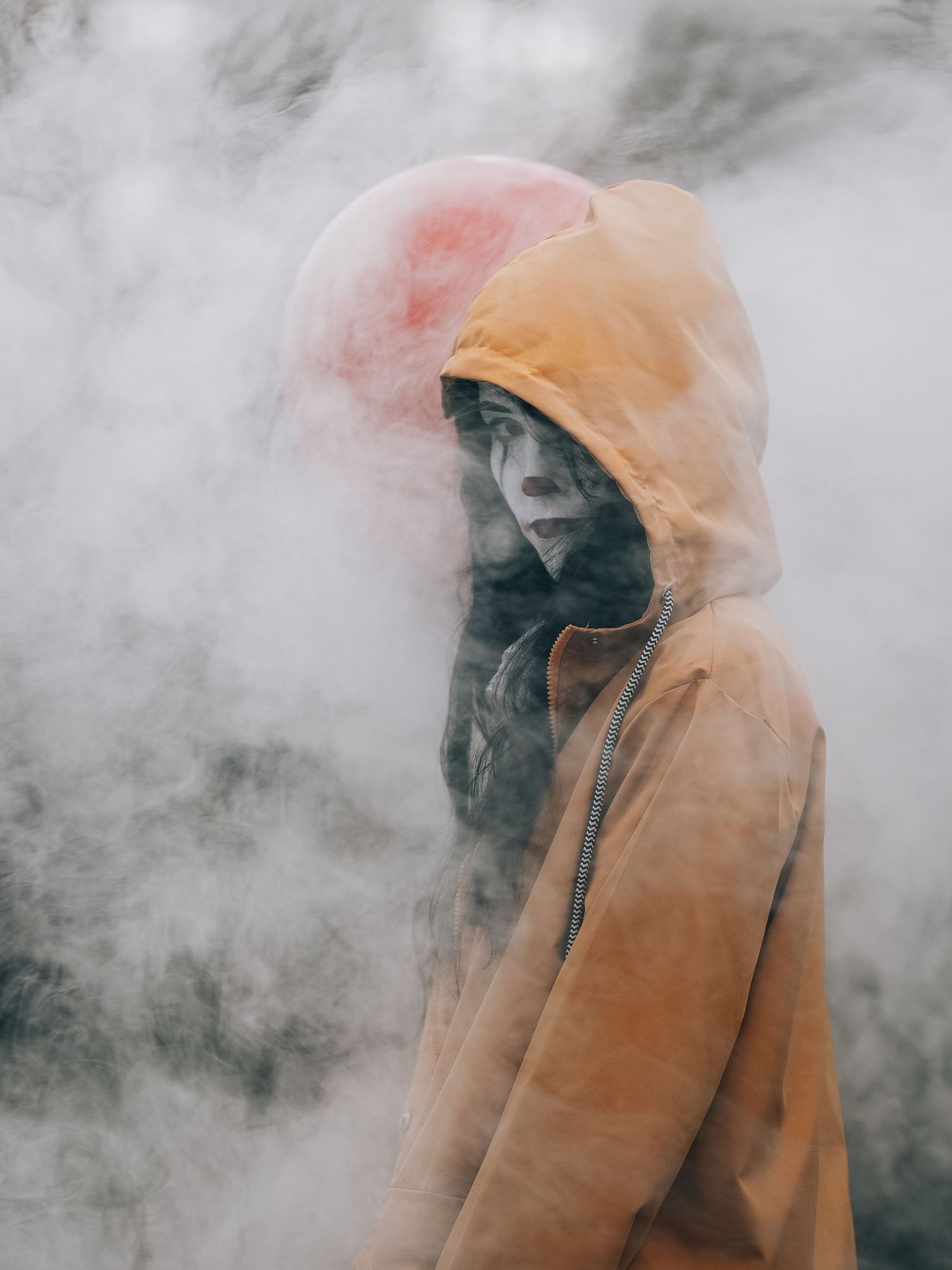 A person wearing an orange hoodie stands surrounded by atmospheric smoke in a dramatic moody scene.