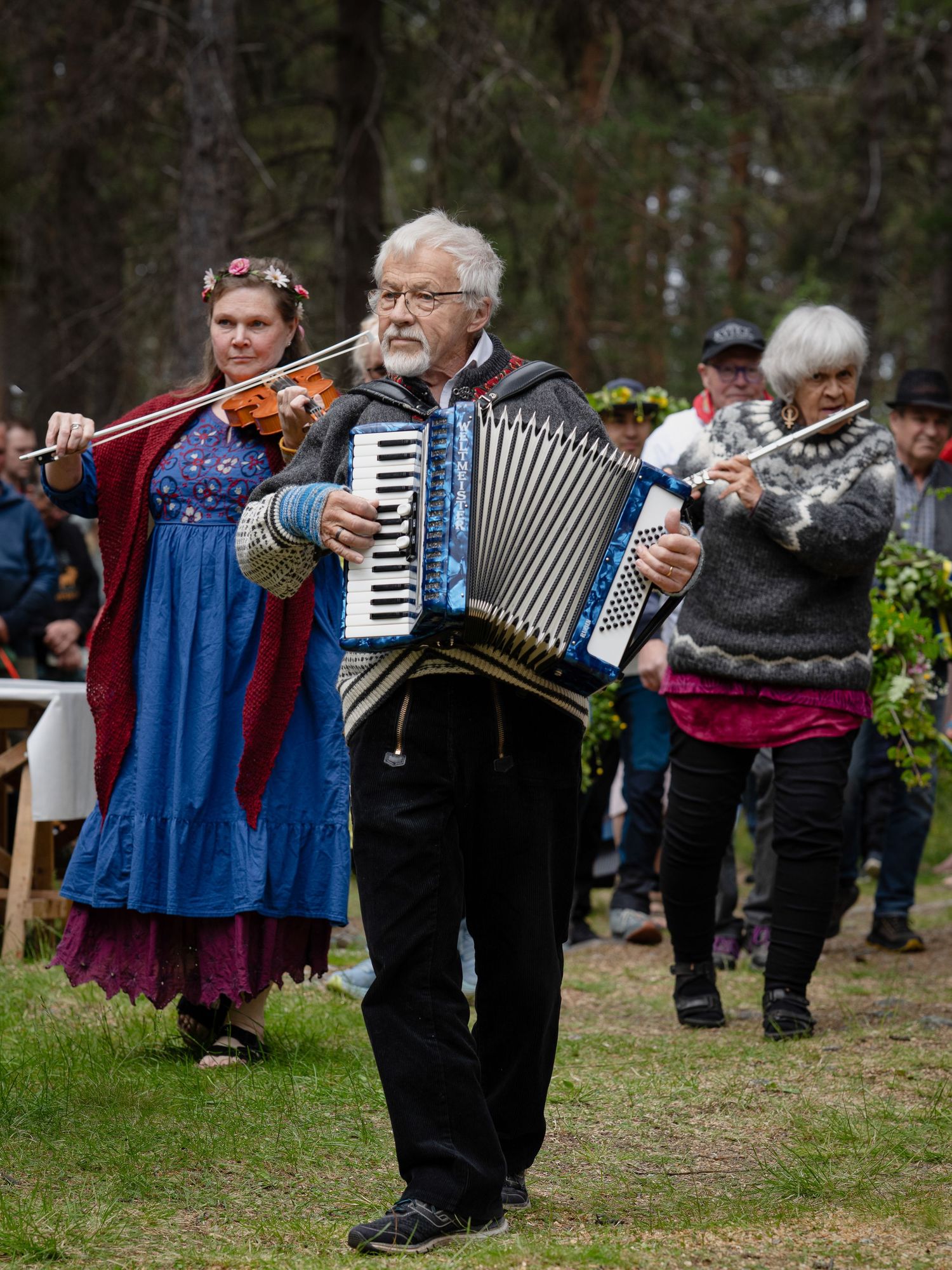 Traditional folk musicians perform outdoors with accordion and violin at a cultural festival in the woods.