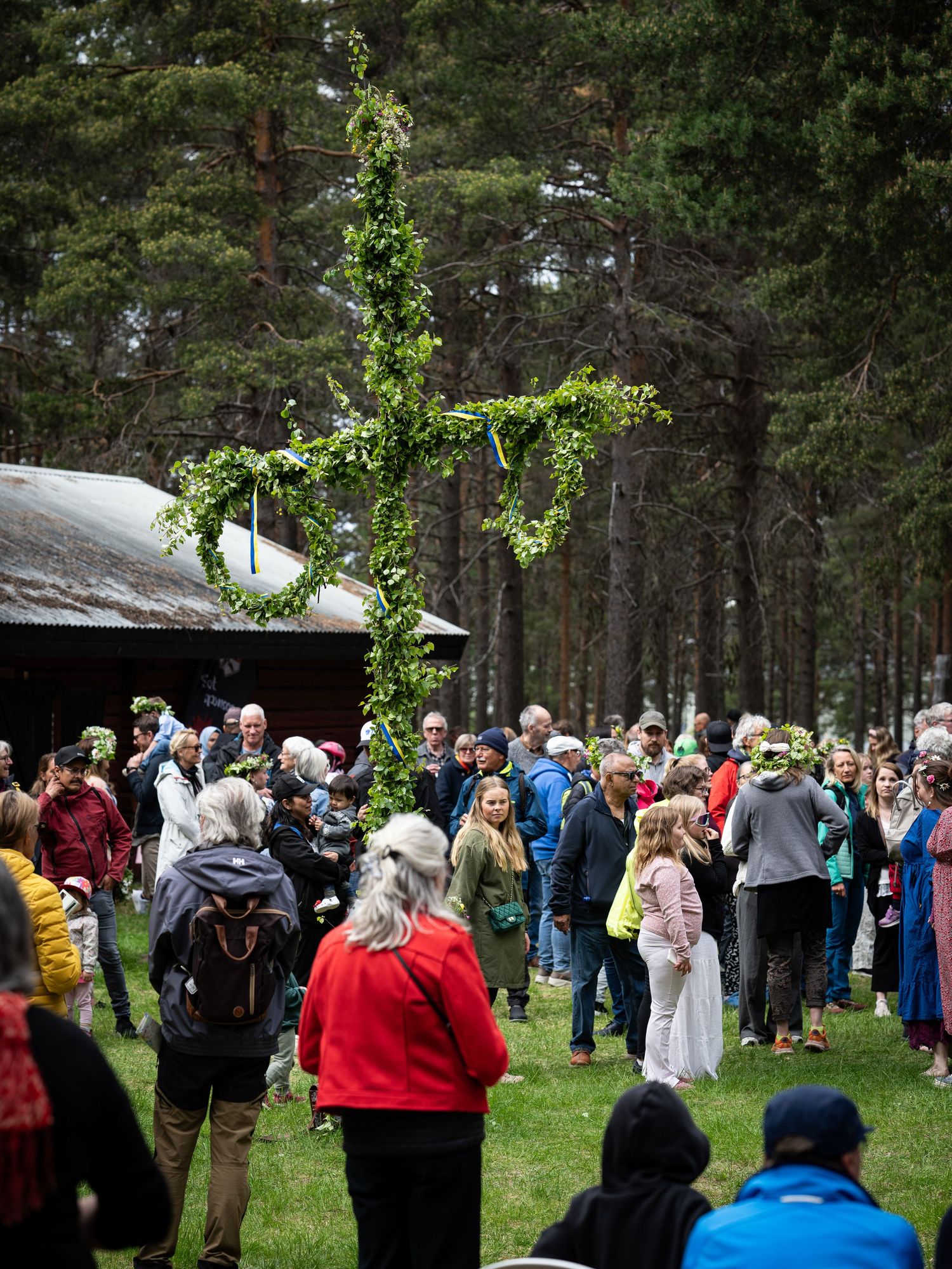 A large crowd gathers outdoors in a forest clearing during what appears to be a festive or ceremonial event.