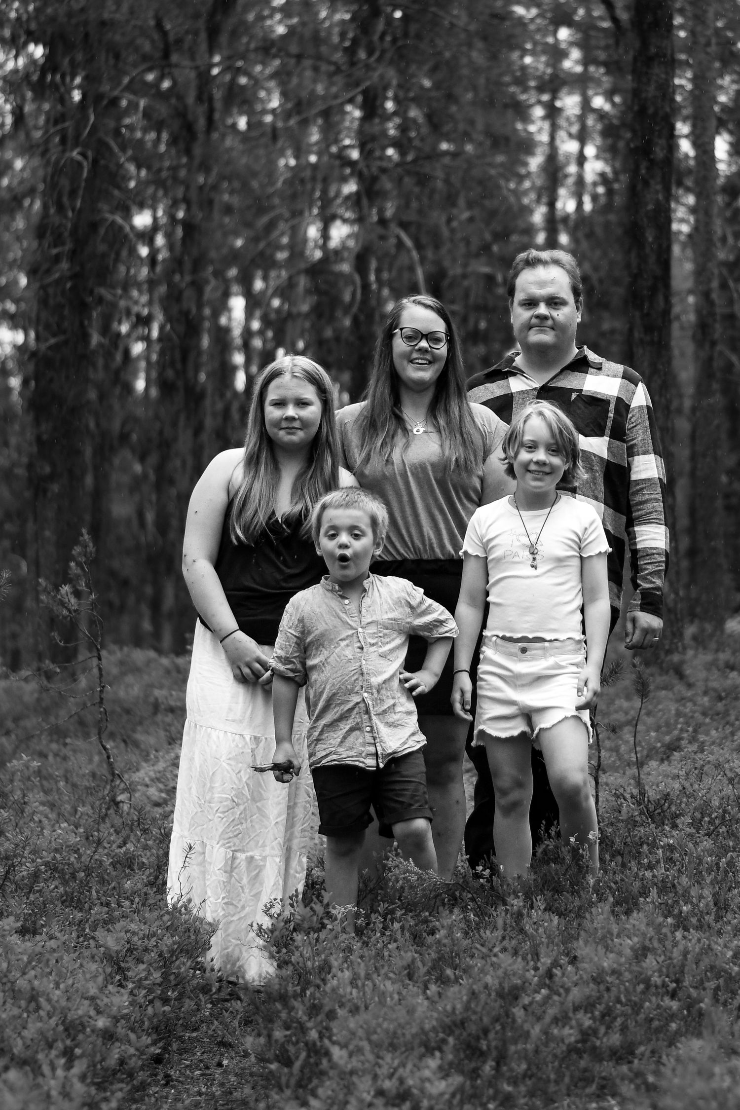 Svartvitt porträtt av en familjegrupp som står tillsammans i en skogsmiljö.